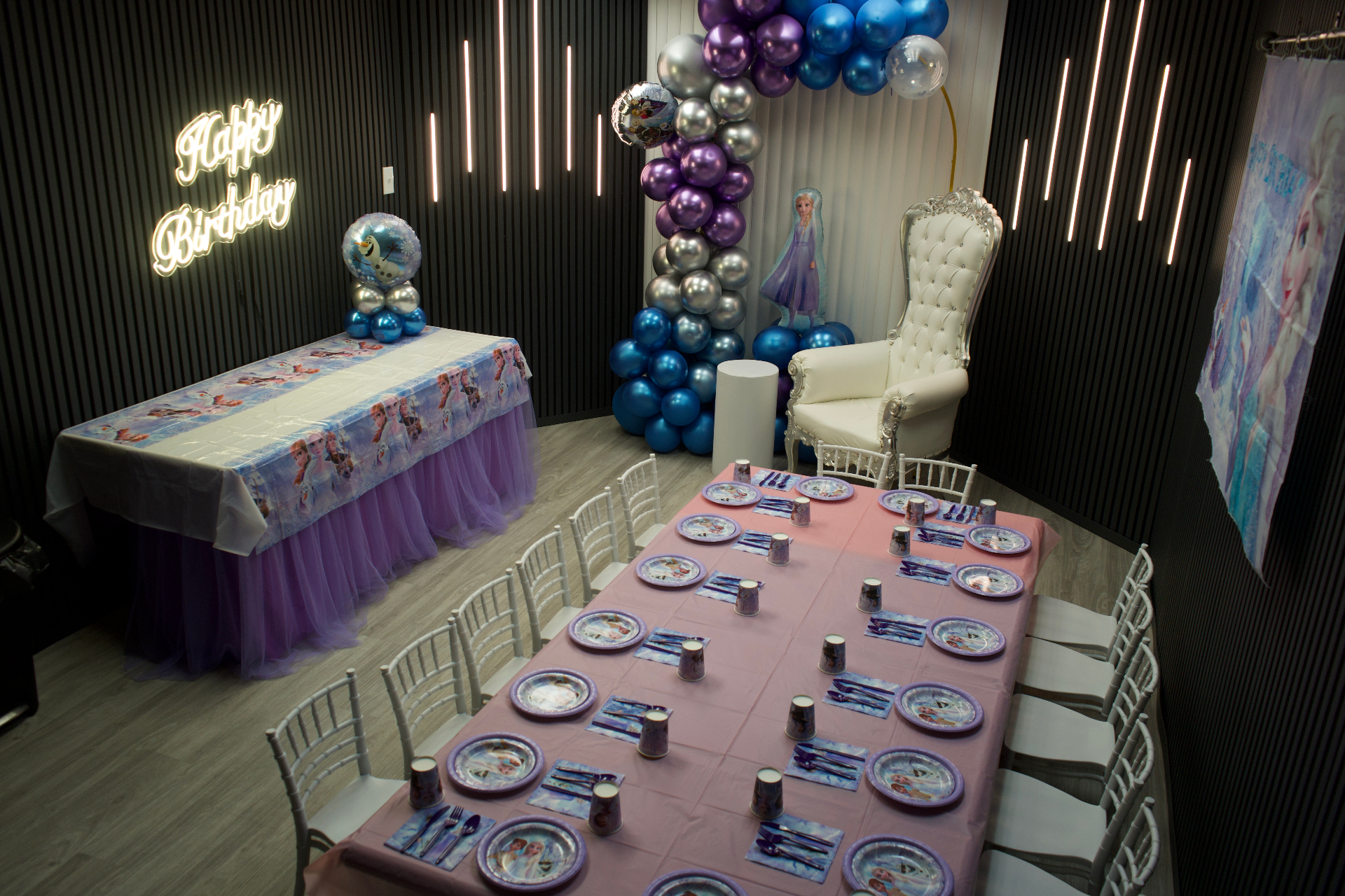 Frozen themed birthday party room with purple and blue balloon arch, Frozen table settings, white throne chair and Happy Birthday neon sign at Star Park
