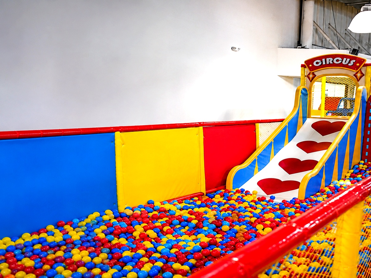 Colorful circus-themed indoor slide with red, yellow and blue panels leading into a ball pit filled with multicolored balls at Star Park
